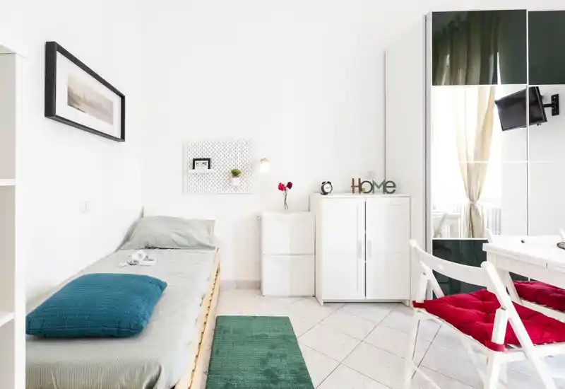 Camera singola luminosa e minimal con letto ben rifatto, armadio con ante a specchio e una piccola scrivania — perfetta per un soggiorno breve e accogliente.