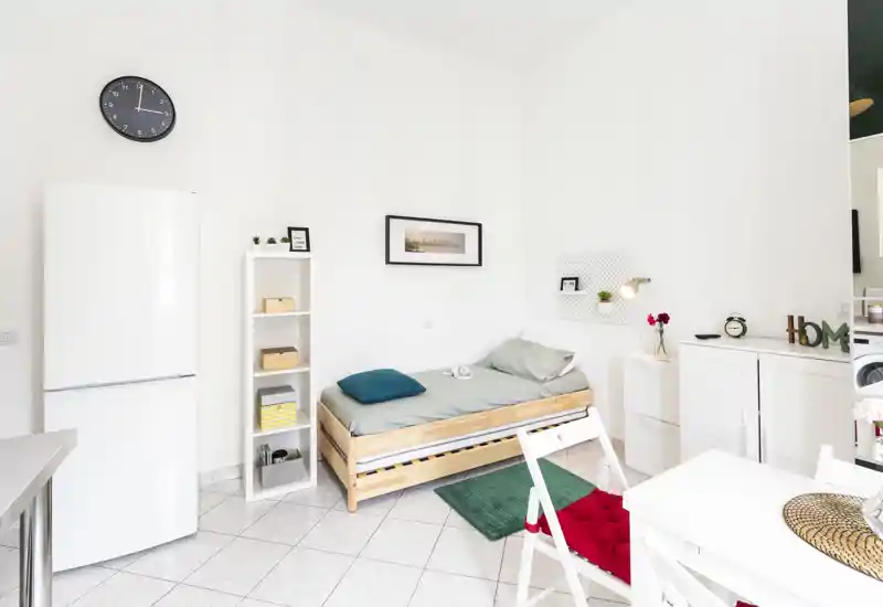 Camera da letto luminosa e compatta con un letto singolo in legno, tessili chiari e contenitori ordinati. Ambiente minimal e arioso, perfetto per una persona o affitti brevi.