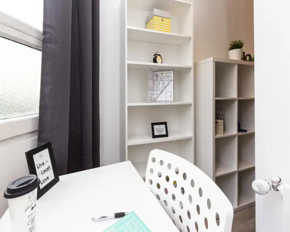 Bright, compact workspace corner with a white desk, modern perforated chair and open shelving — ideal for studying or remote work.