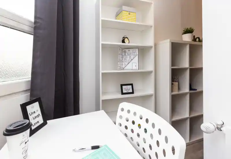 Bright, compact workspace corner with a white desk, modern perforated chair and open shelving — ideal for studying or remote work.