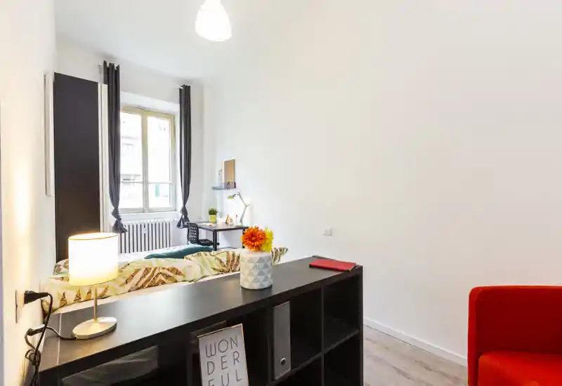 Dormitorio moderno y luminoso con cama estampada, escritorio junto a la ventana y estantería que divide el espacio: bien presentado y acogedor.