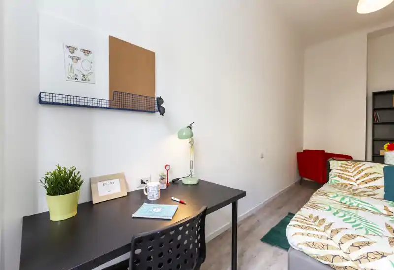 Rincón de dormitorio luminoso y ordenado con cama individual, ropa de cama colorida y un escritorio funcional — ideal para estudiantes o estancias individuales.
