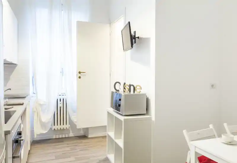 Angolo cucina compatto e luminoso con mobili bianchi, piccolo piano di lavoro, microonde su scaffale e area pranzo: pulito, arioso e accogliente.