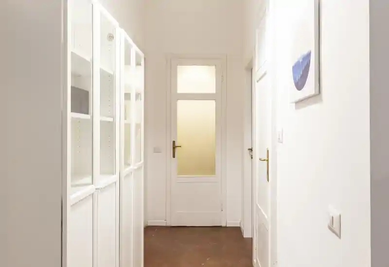 Ingresso luminoso e minimal con pareti bianche, porta con pannello in vetro e armadiature a muro a sinistra — ideale per foto di annuncio che mostrano l'area d'ingresso e il corridoio.