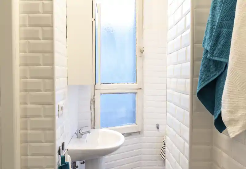 Bagno piccolo e luminoso con piastrelle bianche tipo subway, lavabo a colonna e finestra satinata; gli asciugamani colorati donano un aspetto fresco e curato.