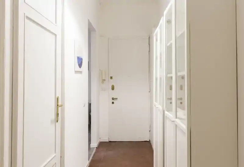 Ingresso luminoso con porta principale bianca, armadi a muro con ante in vetro e pavimento in cotto — uno spazio d'ingresso pulito e accogliente.