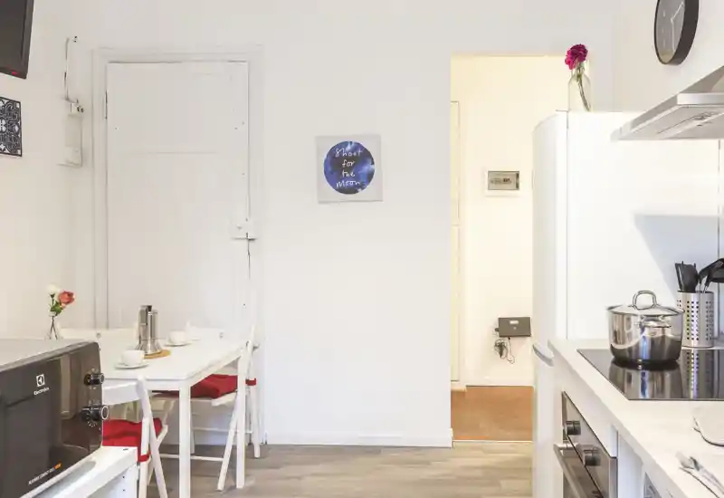 Cucina compatta e luminosa con piano cottura, frigorifero e un piccolo tavolo da pranzo per due — ideale per preparare pasti in un appartamento compatto.