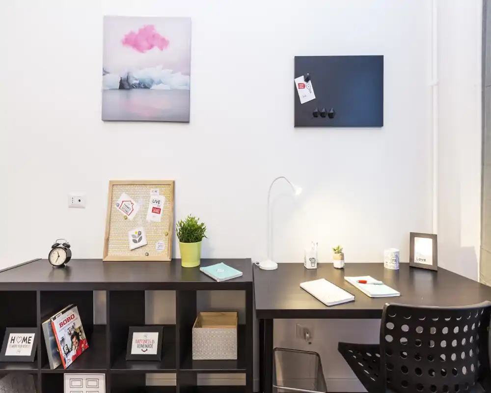Coin bureau lumineux et moderne dans un espace de vie avec bureau foncé, étagères, tableaux décoratifs et lampe de bureau — idéal pour télétravailler ou étudier.