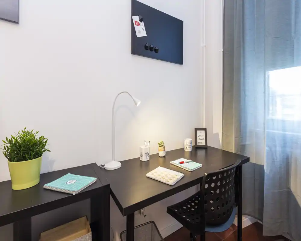 Coin bureau moderne et lumineux avec un bureau noir, lampe, plante décorative et fournitures — un espace de travail confortable bénéficiant de la lumière naturelle de la fenêtre.