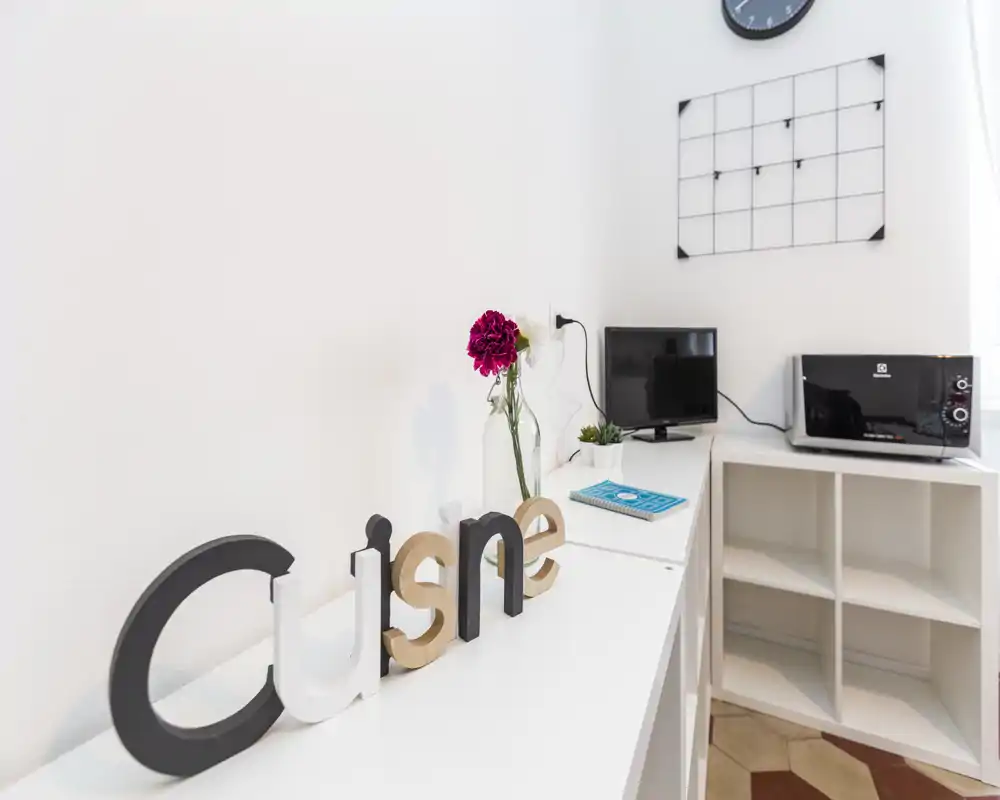 Coin kitchenette compact avec micro-ondes, étagères et détails décoratifs (vase avec fleur et organiseur mural), lumineux et bien rangé.