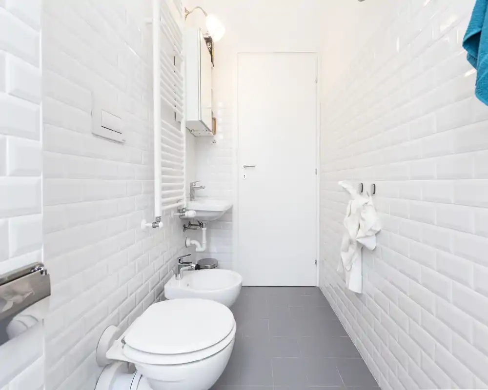 Salle de bains moderne et propre avec carreaux métro blancs, lavabo mural, bidet et WC, et radiateur sèche-serviettes. Espace lumineux, minimaliste et bien entretenu, parfait pour une annonce locative.
