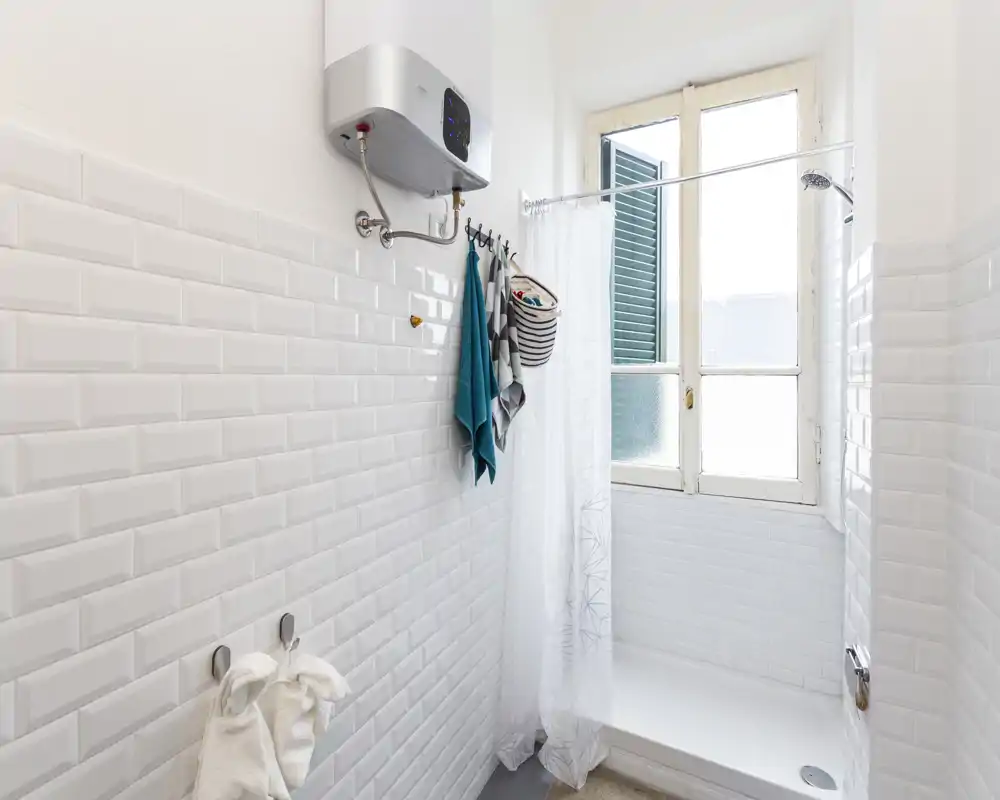 Petite salle de bains lumineuse avec douche à l'italienne, rideau de douche et fenêtre apportant de la lumière naturelle. Carrelage métro blanc et agencement compact adapté à une location.