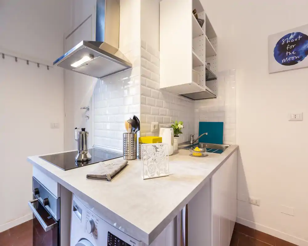 Kitchenette moderne et lumineuse avec plaque à induction, hotte inox, évier intégré et petits appareils sur le plan de travail; décoration soignée et rangements pratiques.