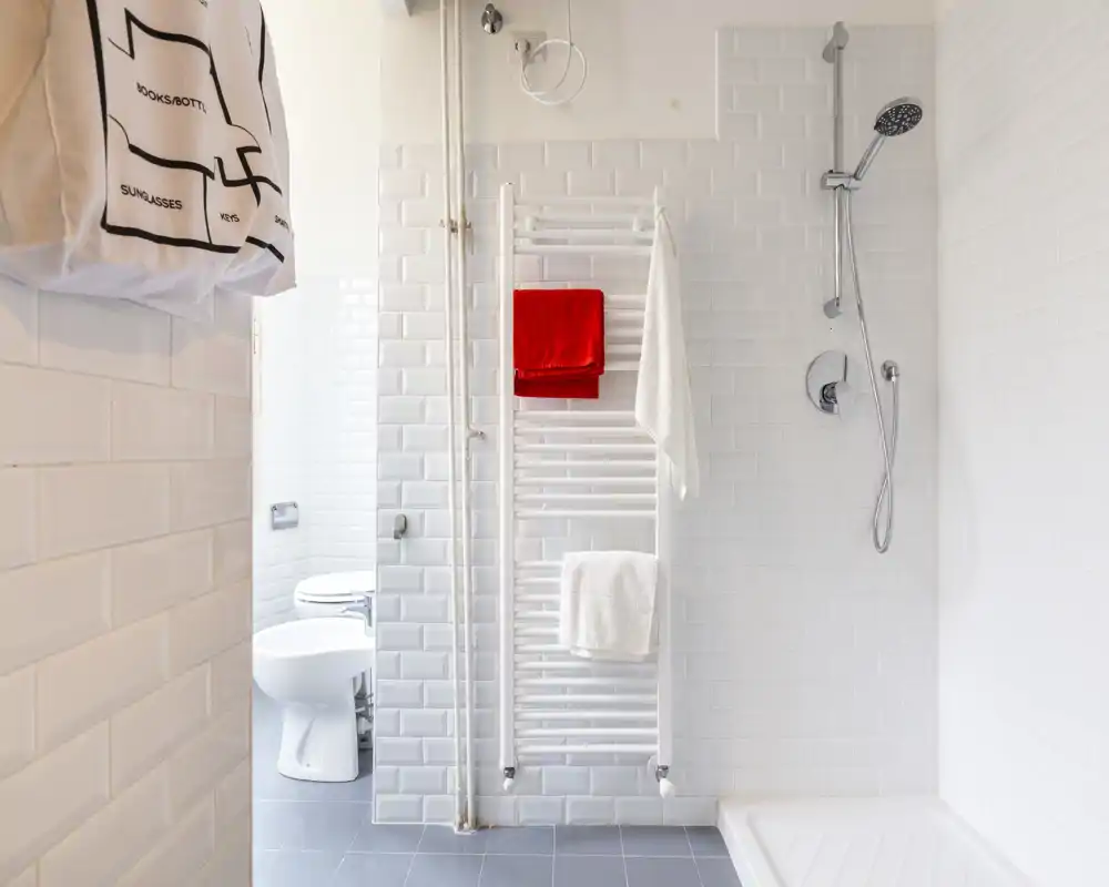 Salle de bains moderne et lumineuse avec carrelage blanc métro, douche murale et radiateur porte-serviettes; ambiance propre et minimaliste adaptée à une annonce.
