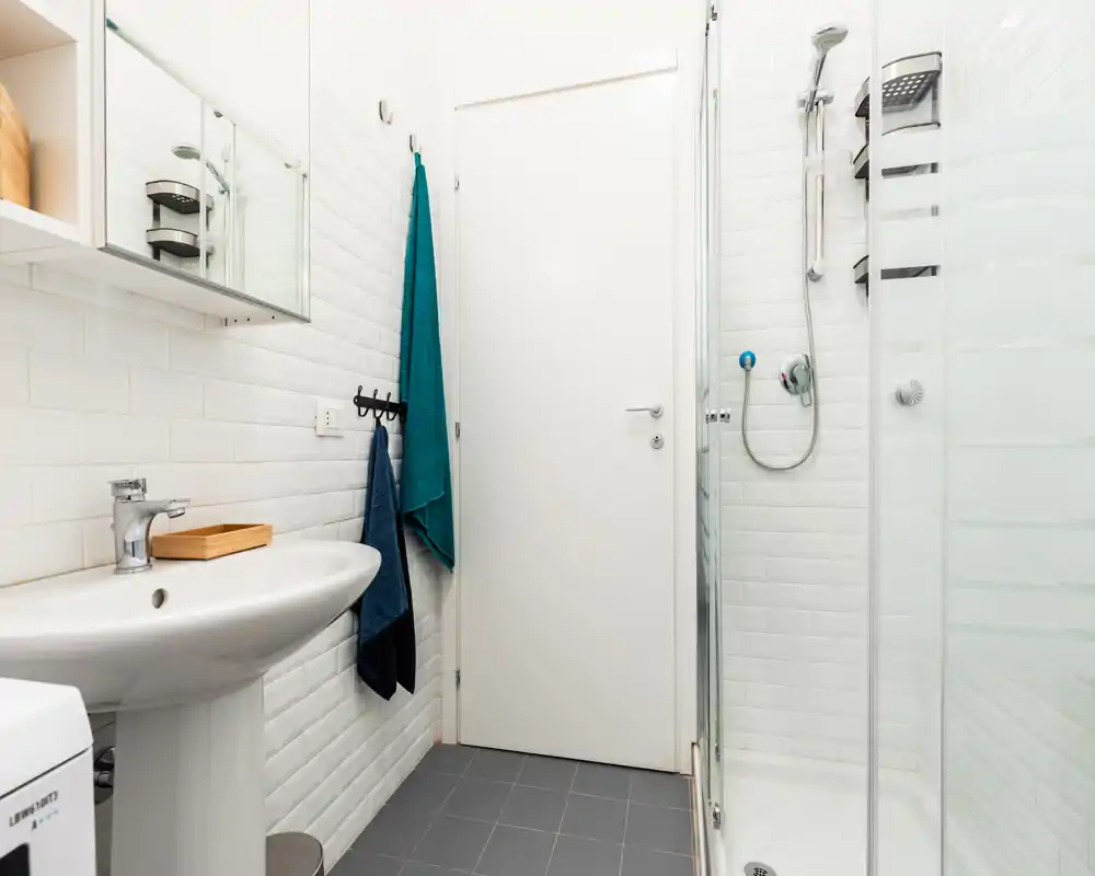 Salle de bains moderne et lumineuse avec douche d'angle, lavabo sur colonne et carrelage blanc métro — propre et bien éclairée.