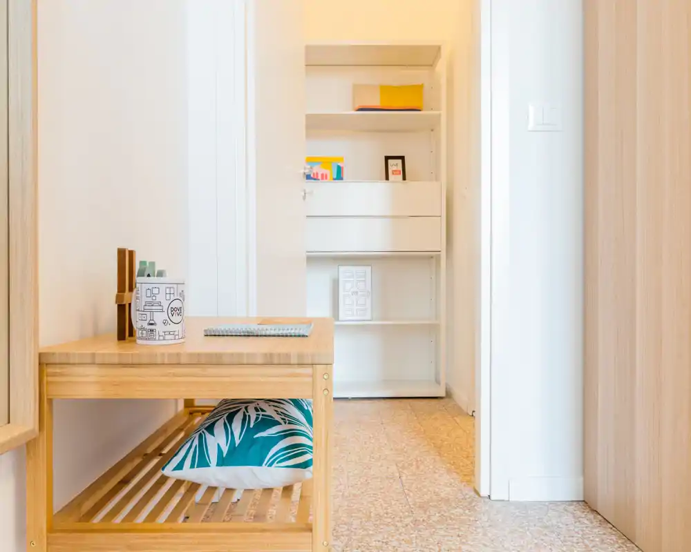 Entrée lumineuse et soignée avec banc en bois, coussin décoratif et étagères visibles au fond du couloir — un espace d'accueil minimaliste et chaleureux.