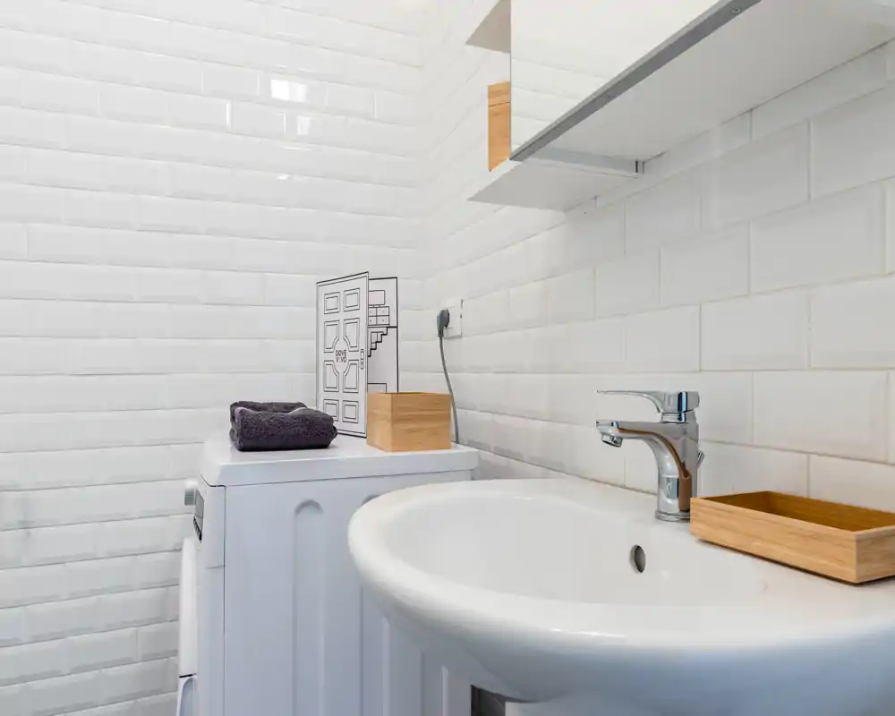 Petite salle de bain moderne avec carrelage blanc façon métro, lavabo sur colonne et machine à laver ; lumineuse, propre et sobre.
