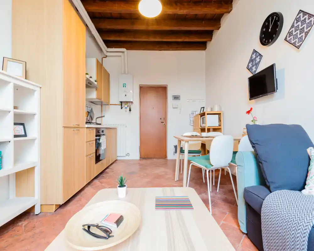 Espace de vie lumineux et bien agencé ouvert sur une kitchenette, avec un canapé confortable — parfait pour de courts séjours. Plafond à poutres apparentes et mobilier moderne et simple pour un appartement chaleureux.
