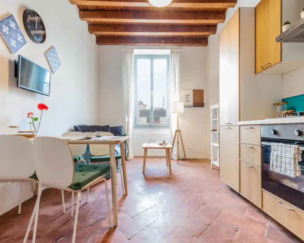 Espace de vie lumineux et chaleureux avec petite table à manger et kitchenette intégrée. Les poutres apparentes et le sol en terre cuite ajoutent du caractère.