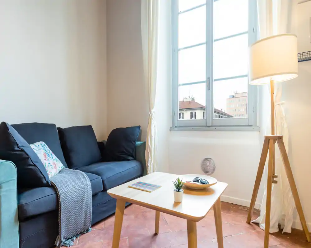 Coin salon lumineux et chaleureux avec un canapé foncé, une table basse en bois, une lampe sur pied et une grande fenêtre apportant la lumière naturelle.