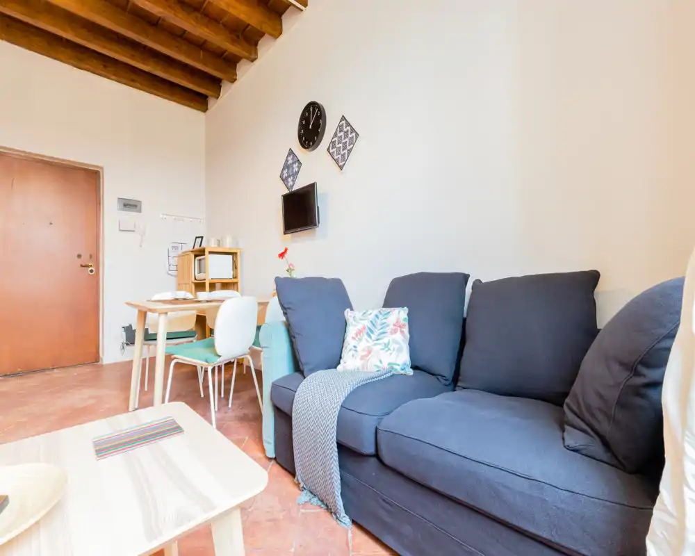 Espace de vie lumineux et confortable avec un canapé bleu marine, coussins décoratifs et un coin repas — idéal pour se détendre et prendre un repas informel.