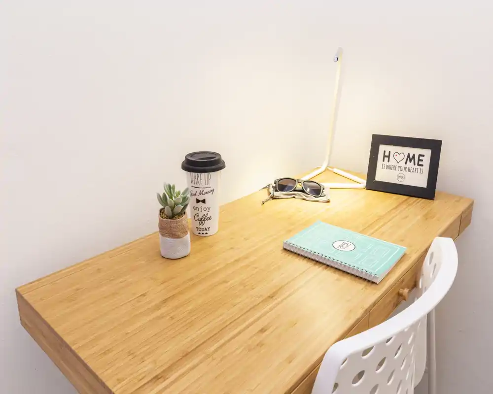 Angolo scrivania luminoso e ordinato con piano in legno, piccola pianta, lampada e cornice decorativa — un ambiente accogliente per leggere o lavorare da remoto.