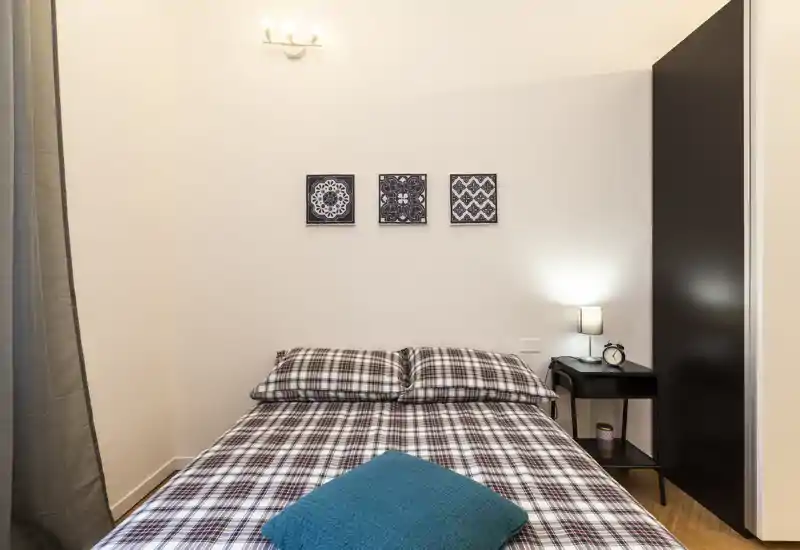 Chambre lumineuse et stylée avec lit double en linge à carreaux, table de chevet avec lampe et décorations murales — chaleureuse et accueillante.