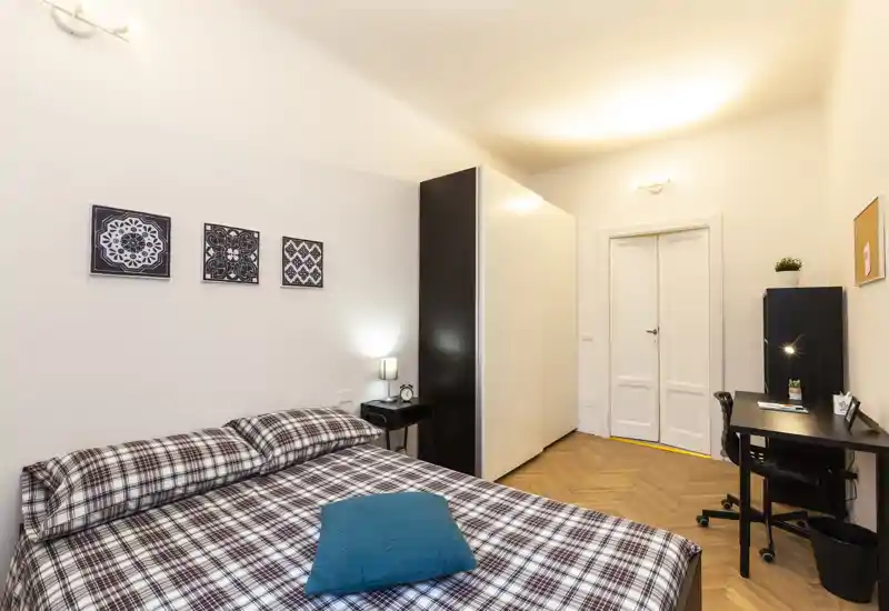 Chambre lumineuse et bien aménagée avec un grand lit double, linge à carreaux et un petit espace bureau — idéale pour une personne seule ou un couple.