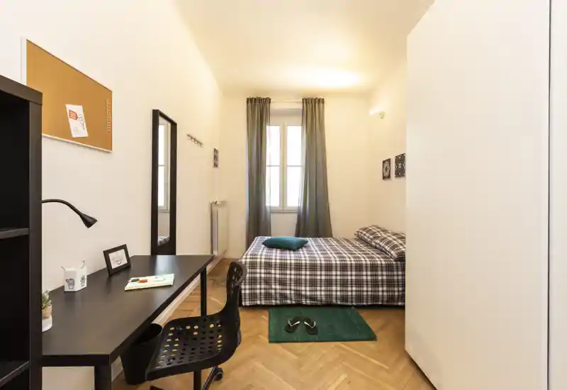 Chambre simple lumineuse et bien aménagée avec lit à carreaux, bureau et lumière naturelle douce — idéale pour étudiant ou professionnel.