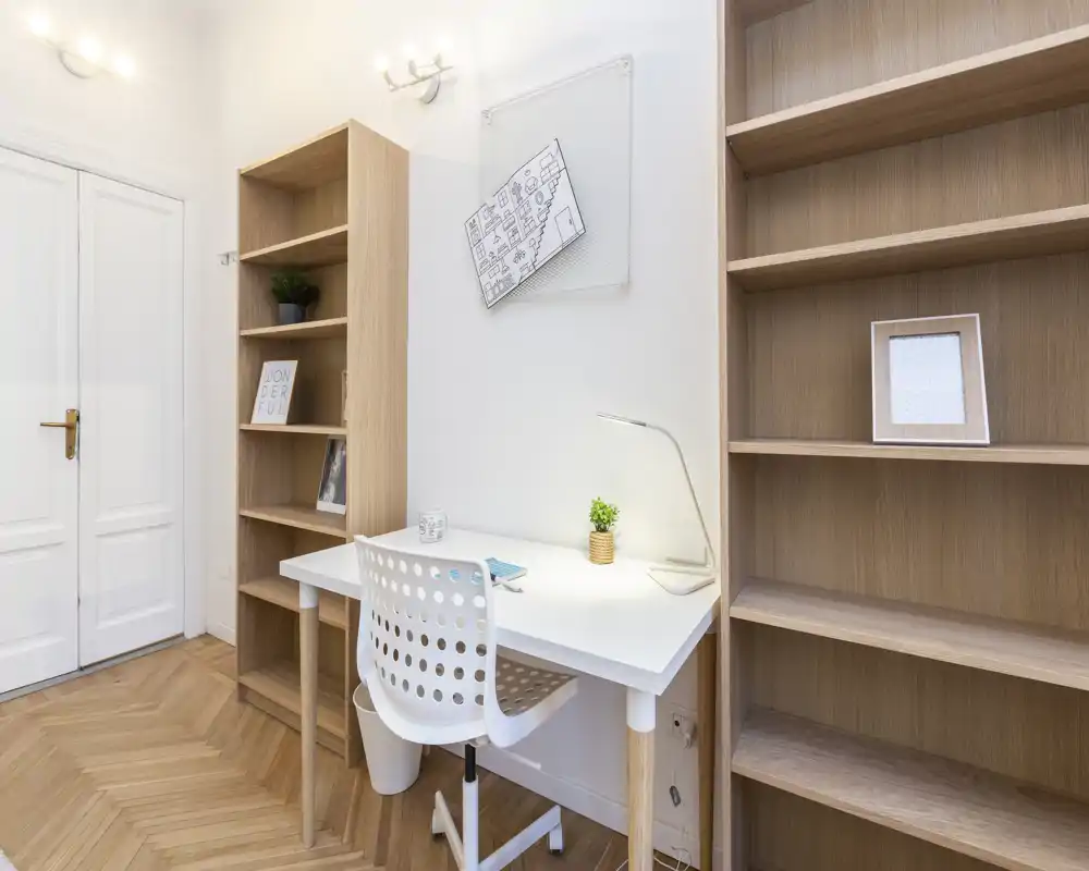 Rincón de trabajo luminoso y minimalista con escritorio blanco, silla perforada y estanterías de madera — ideal para teletrabajo o estudio.
