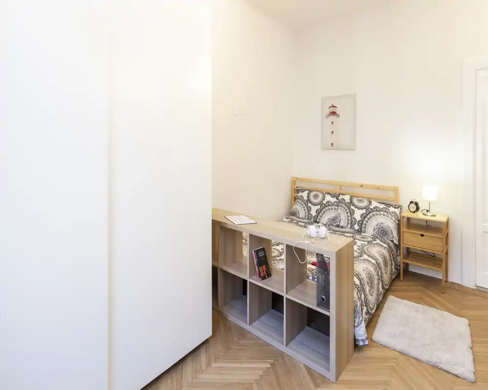 Dormitorio luminoso y ordenado con cama doble estampada, mesita de noche y alfombra suave — ideal para alquileres de corta temporada.