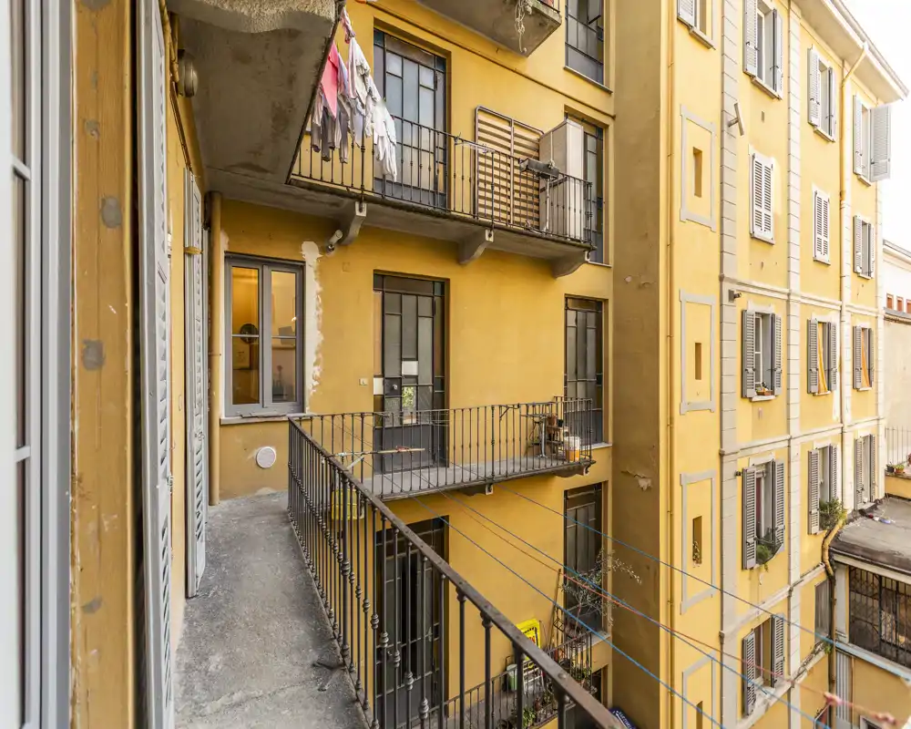 Vista esterna di un balcone stretto su un cortile interno con facciate gialle e ringhiere in metallo; perfetto per un piccolo spazio esterno in un appartamento cittadino.