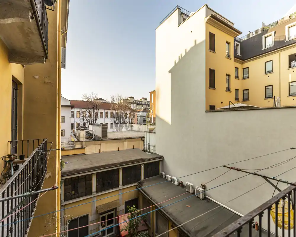 Vista dal balcone su un cortile interno con edifici gialli, tetti e fili per stendere: luminoso affaccio urbano adatto a immobili in città.