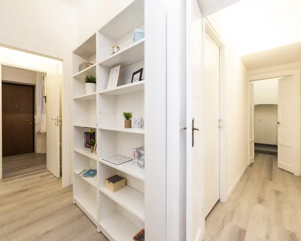 Ingresso luminoso e moderno con pavimento in legno chiaro e scaffalatura bianca integrata; linee pulite e decorazioni neutre offrono un'accoglienza elegante.