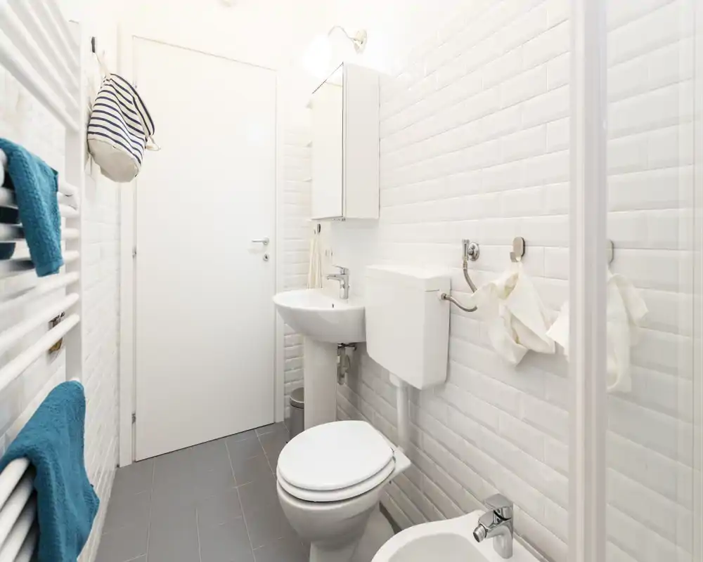 Bagno luminoso e moderno con piastrelle bianche a metro, lavabo a colonna, WC e bidet; gli asciugamani ordinati danno un tocco fresco.