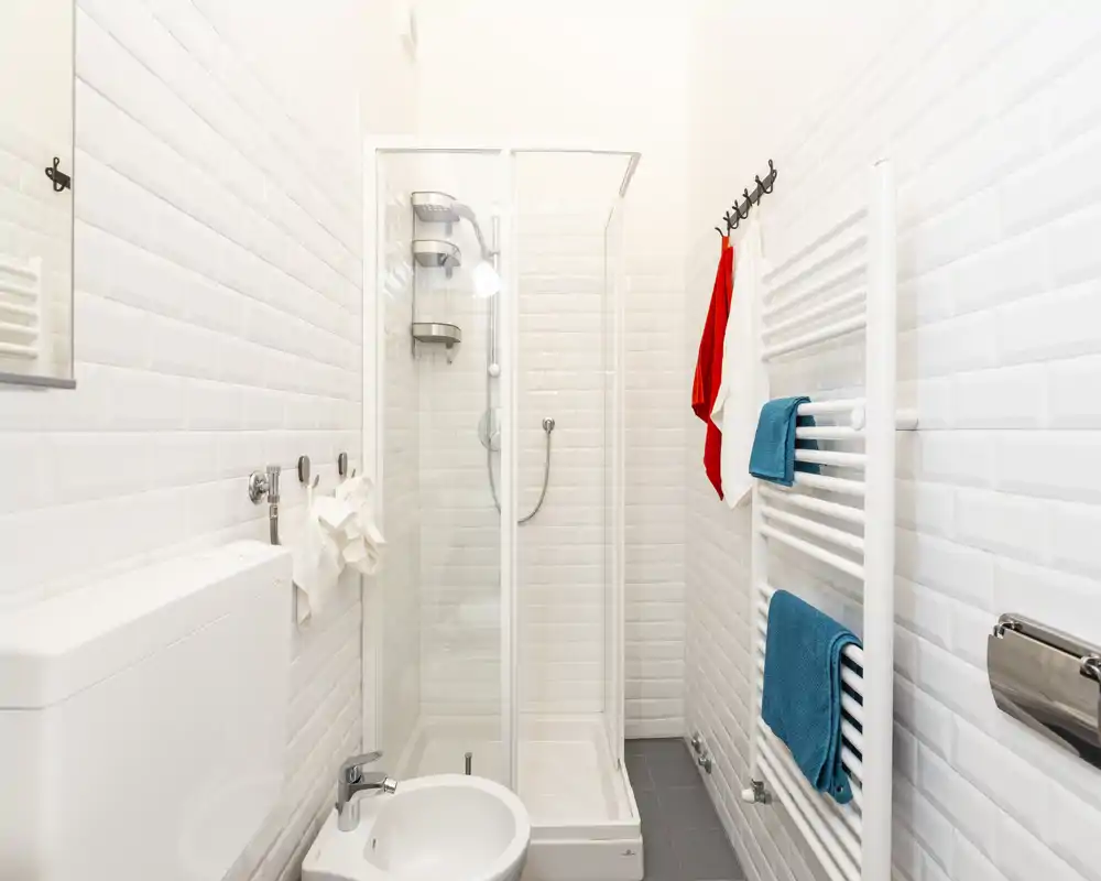 Bagno compatto e moderno con doccia con box in vetro, piastrelle bianche effetto subway e termoarredo con asciugamani colorati.