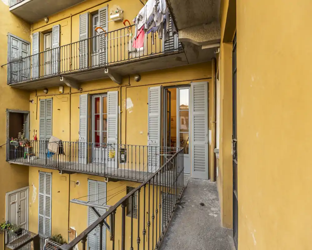 Corridoio esterno/balcone soleggiato di un condominio con ringhiere in metallo, persiane e panni stesi — ideale per mostrare l'accesso esterno e il carattere urbano.
