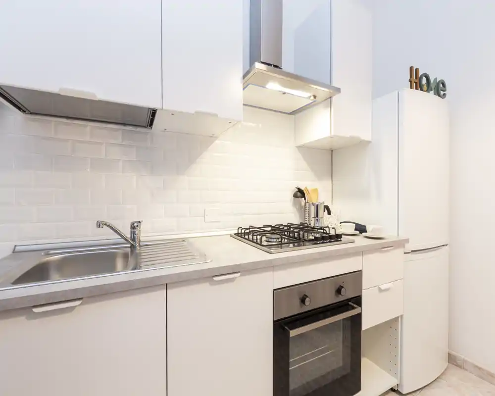 Cucina moderna e luminosa con mobili bianchi, lavello in acciaio, piano cottura a 4 fuochi e forno incassato — design pulito e minimal ideale per annunci.