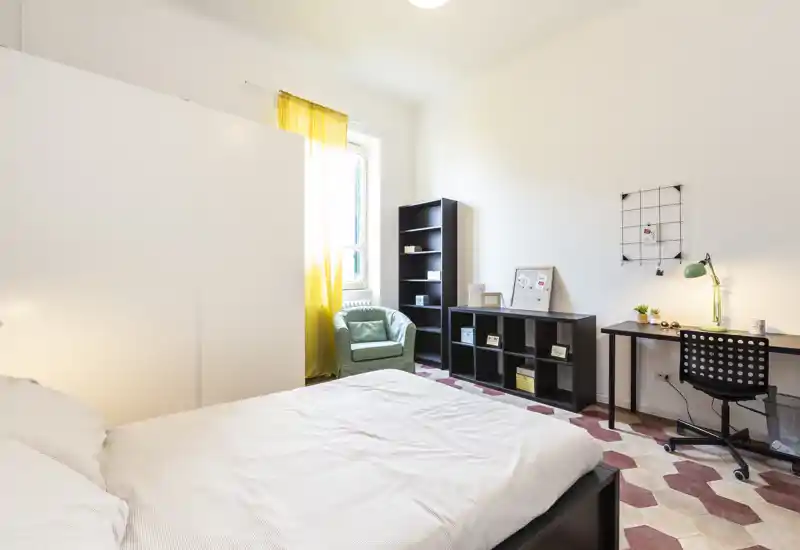 Dormitorio luminoso y bien decorado con cama doble cómoda, zona de escritorio y estanterías; la cortina amarilla y el suelo con motivos aportan personalidad.