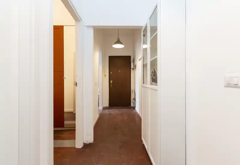 Ingresso luminoso con porta d'ingresso in legno, pavimento in cotto esagonale e lampada a sospensione—spazio pulito e accogliente.