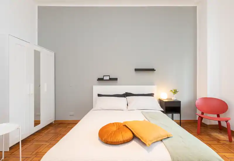 Camera da letto moderna e luminosa con letto matrimoniale centrale, tessili morbidi e comodino con lampada: stile pulito e minimale perfetto per annunci.