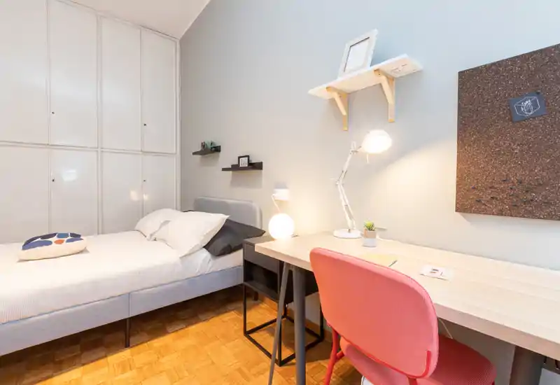 Camera singola moderna e luminosa con letto comodo, lampade da comodino e una scrivania funzionale — ideale per uno studente o un professionista.