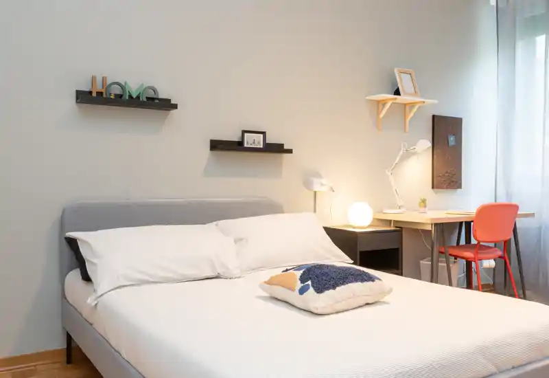 Camera da letto moderna e luminosa con letto matrimoniale, cuscini accoglienti e una piccola scrivania vicino alla finestra — ideale per una o due persone.