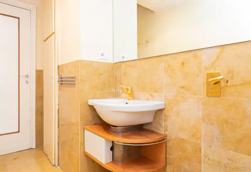 Compact bathroom with a wall-mounted sink, warm beige tiles and a large mirror — bright and clean, suitable for a rental listing.