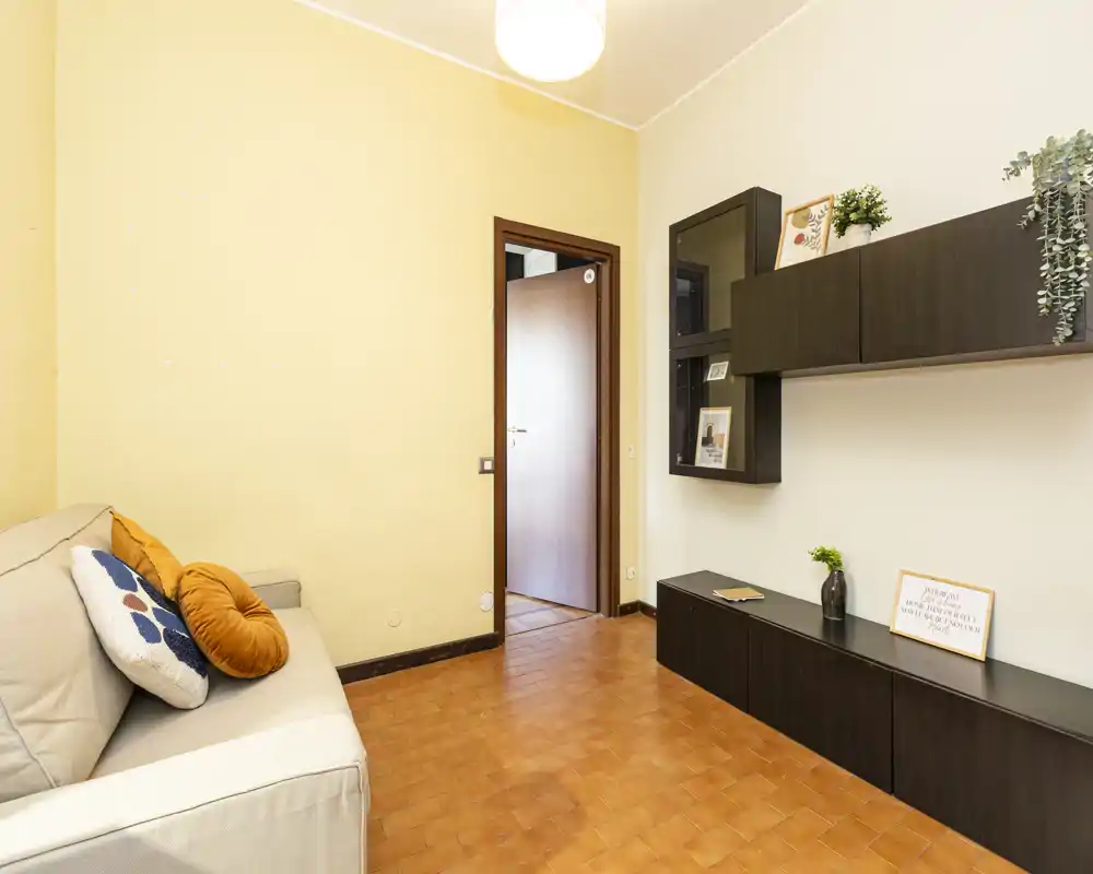 Bright, simply styled living room with a compact sofa, cushions and modern wall-mounted storage — ideal for a cozy, low-maintenance apartment.