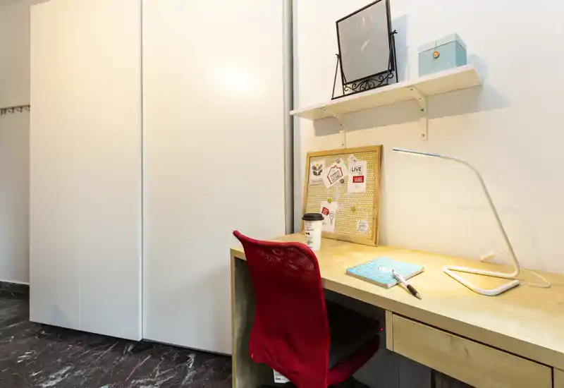 Spazio di lavoro funzionale accanto all'armadio: scrivania in legno con lampada moderna, bacheca e sedia ergonomica rossa, ideale per smart working o studio.