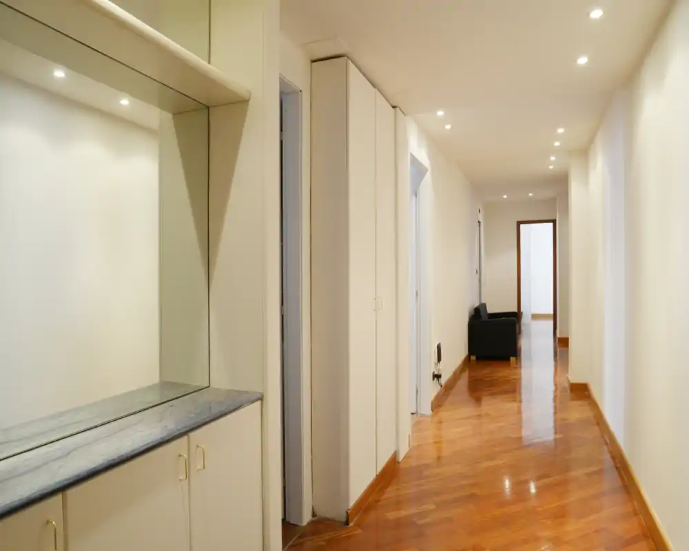 Corridoio luminoso con mobile incorporato e grande specchio; faretti incassati e pavimento in legno lucido creano un ingresso pulito e accogliente.