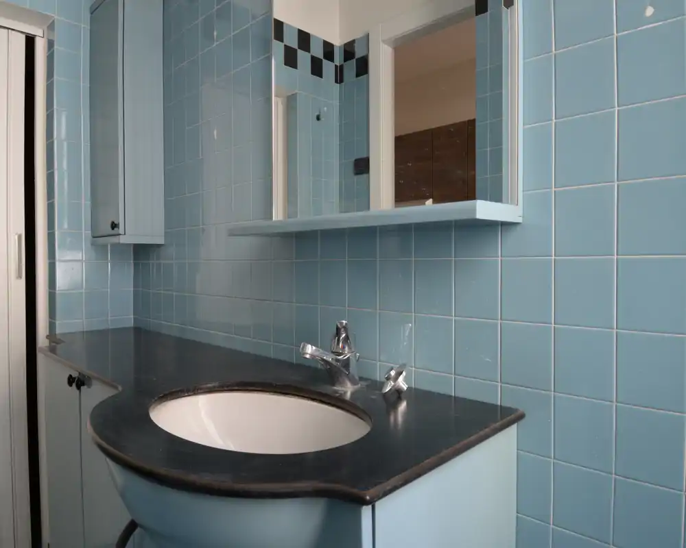 Bagno piastrellato chiaro con lavabo incassato su top nero, rubinetteria cromata e mobili blu coordinati; immagine nitida e ben illuminata adatta all'annuncio.