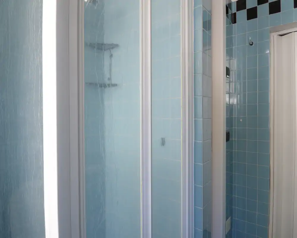 Doccia compatta in bagno con piastrelle ceramiche azzurro chiaro e porta a vetro incorniciata; ambiente pulito e ben illuminato adatto agli annunci.