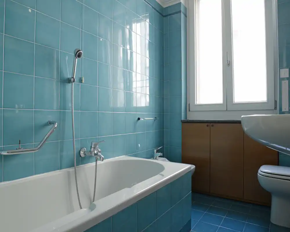 Bagno luminoso con vasca, doccia a mano, lavabo e WC; piastrelle turchesi e luce naturale da una finestra ampia danno una sensazione di pulizia e freschezza.